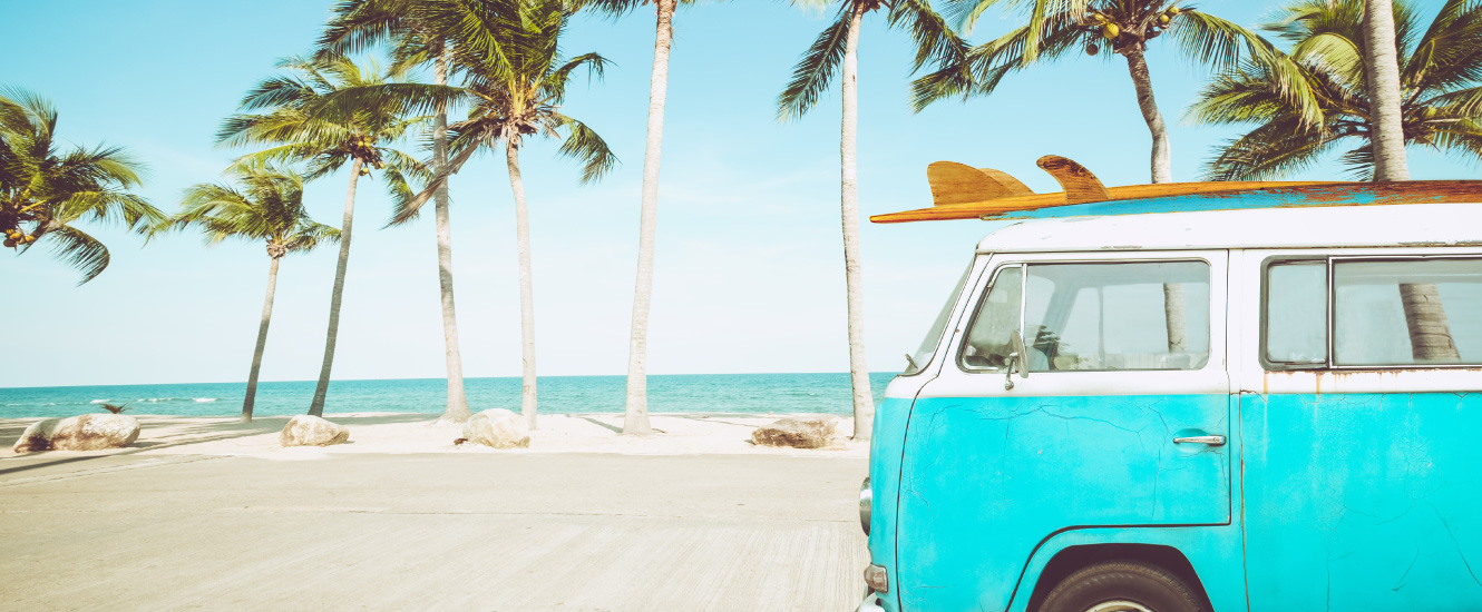 teal VW bus with surfboards in front of palm trees and ocean