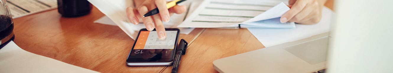 close up of someone using a phone with calculator and papers around