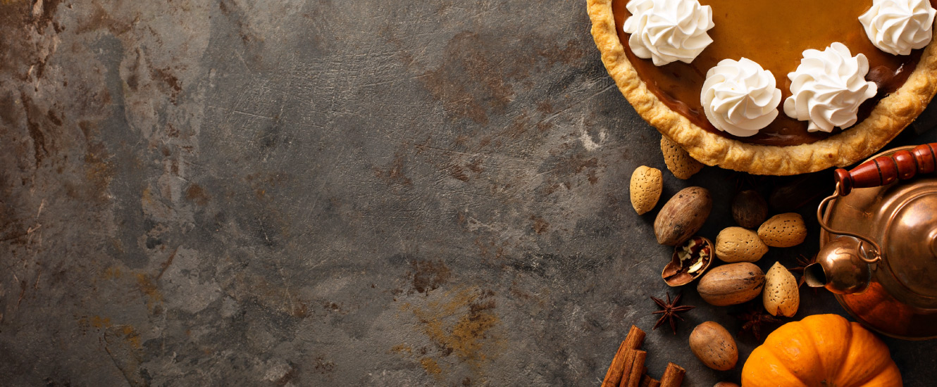 pumpkin pie, nuts, tea kettle, pumpkin, and cinnamon on a dark stone background